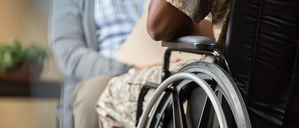 njured African American veteran in wheelchair talks with military psychiatrist. Both men are seen from the neck down. Focus is on the wheelchair.