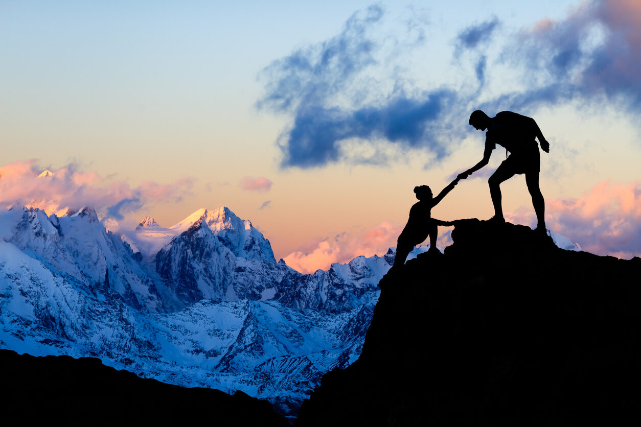 Teamwork couple helping hand, trust in mountains. Team of climbers man and woman hiking, help each other on top of mountain, climbing together, inspiring sunset on Elbrus, Russia.