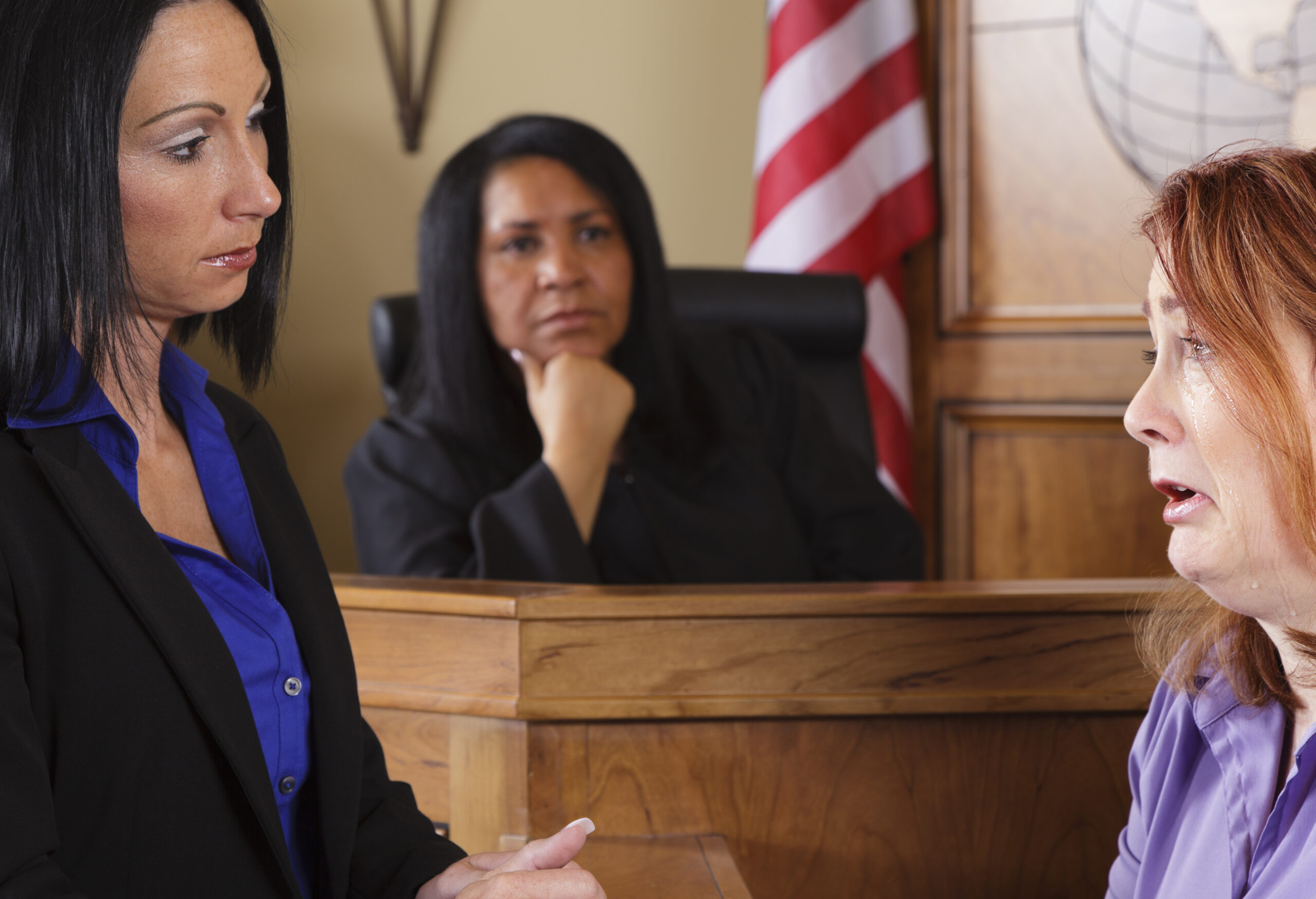A crying witness in a courtroom with the judge in the out-of-focus background.