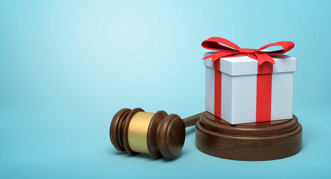 3d rendering of white gift box with red ribbon on round wooden block and brown wooden gavel on blue background. Digital art. Objects and materials. Gifts and celebrations.